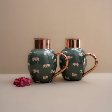 Two green ceramic mugs with copper handles on a beige surface.