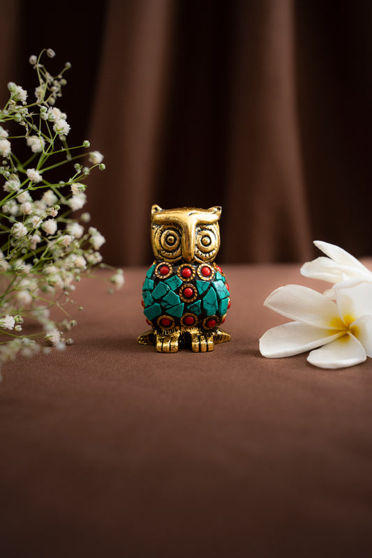 Decorative owl figurine with gemstones on a brown surface with flowers.