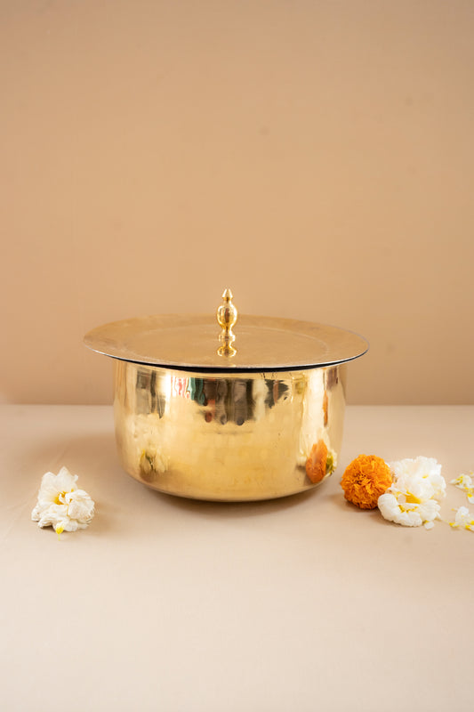 Gold cake stand with a lid on a beige surface with decorative flowers.