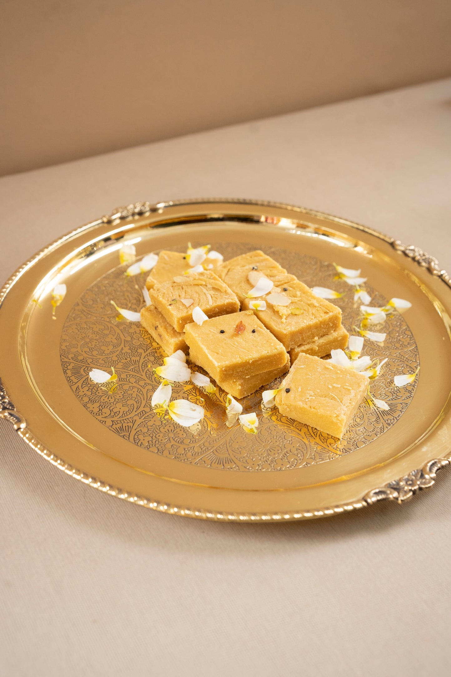 Square pieces of a yellow dessert on a decorative gold plate with white flowers.