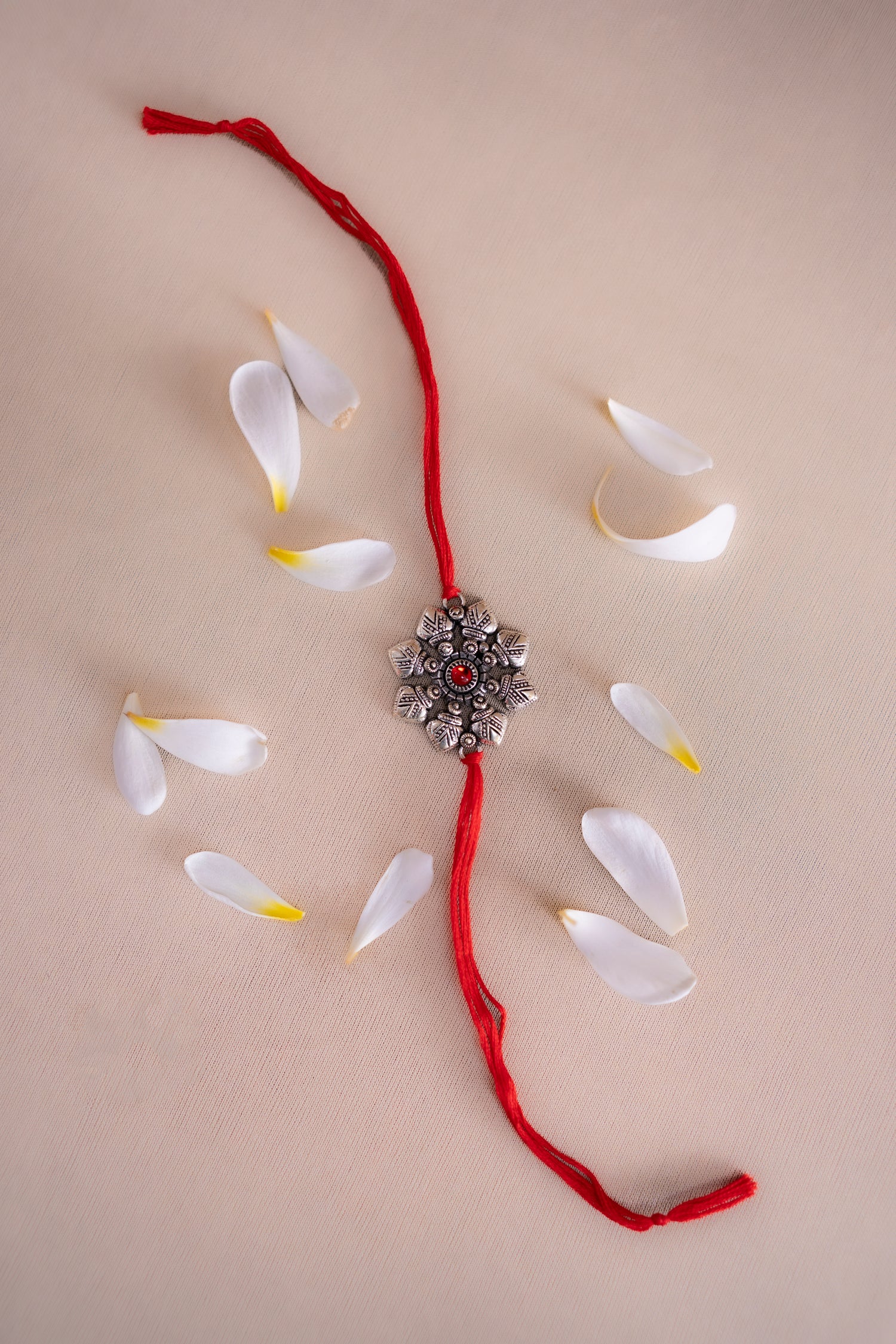 Red thread with a silver decorative element on a beige background with white petals.