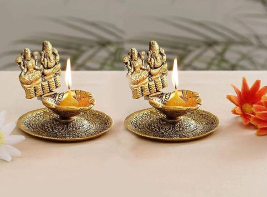 Two ornate brass diya lamps with lit candles on a light background