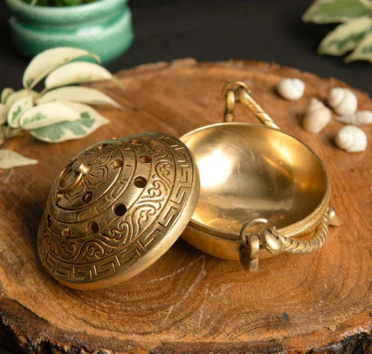 Brass incense burner with intricate designs on a wooden surface with plants in the background