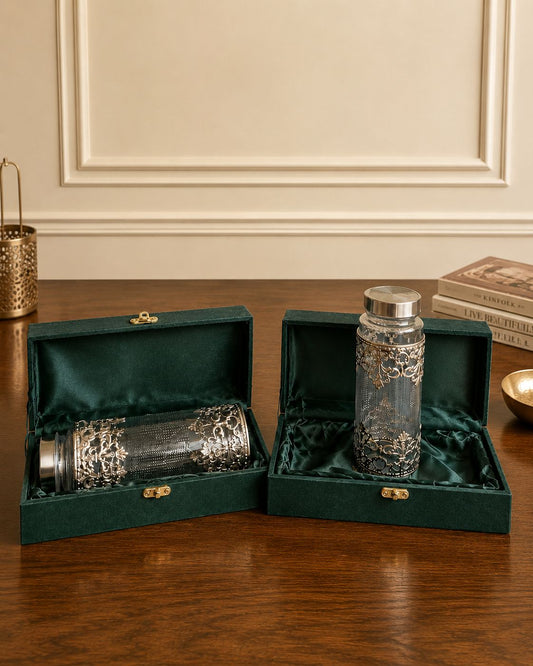 Two glass bottles with silver caps in green velvet boxes on a wooden surface.