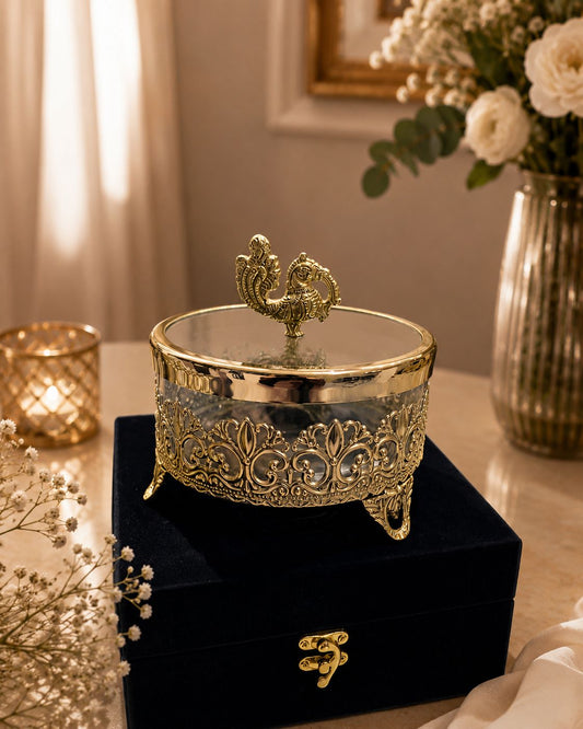 Decorative gold jewelry box on a black stand with flowers and candles in the background