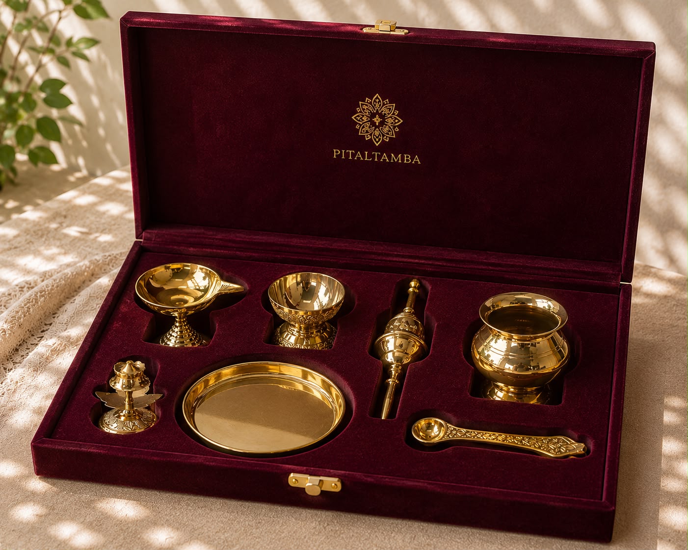 Pitaltamba brass and gold-toned ceremonial set displayed inside an open deep burgundy velvet gift box, with the brand name printed in gold on the inside lid.
