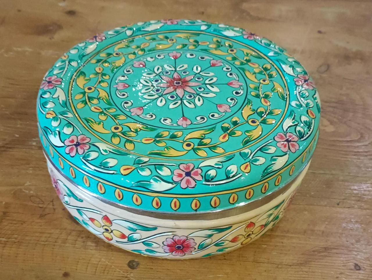 Decorative round box with floral patterns on a wooden surface