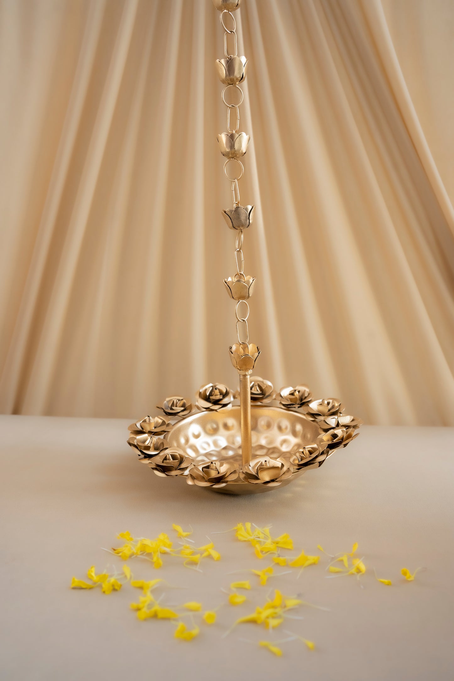 Gold decorative hanging item with yellow petals on a beige background