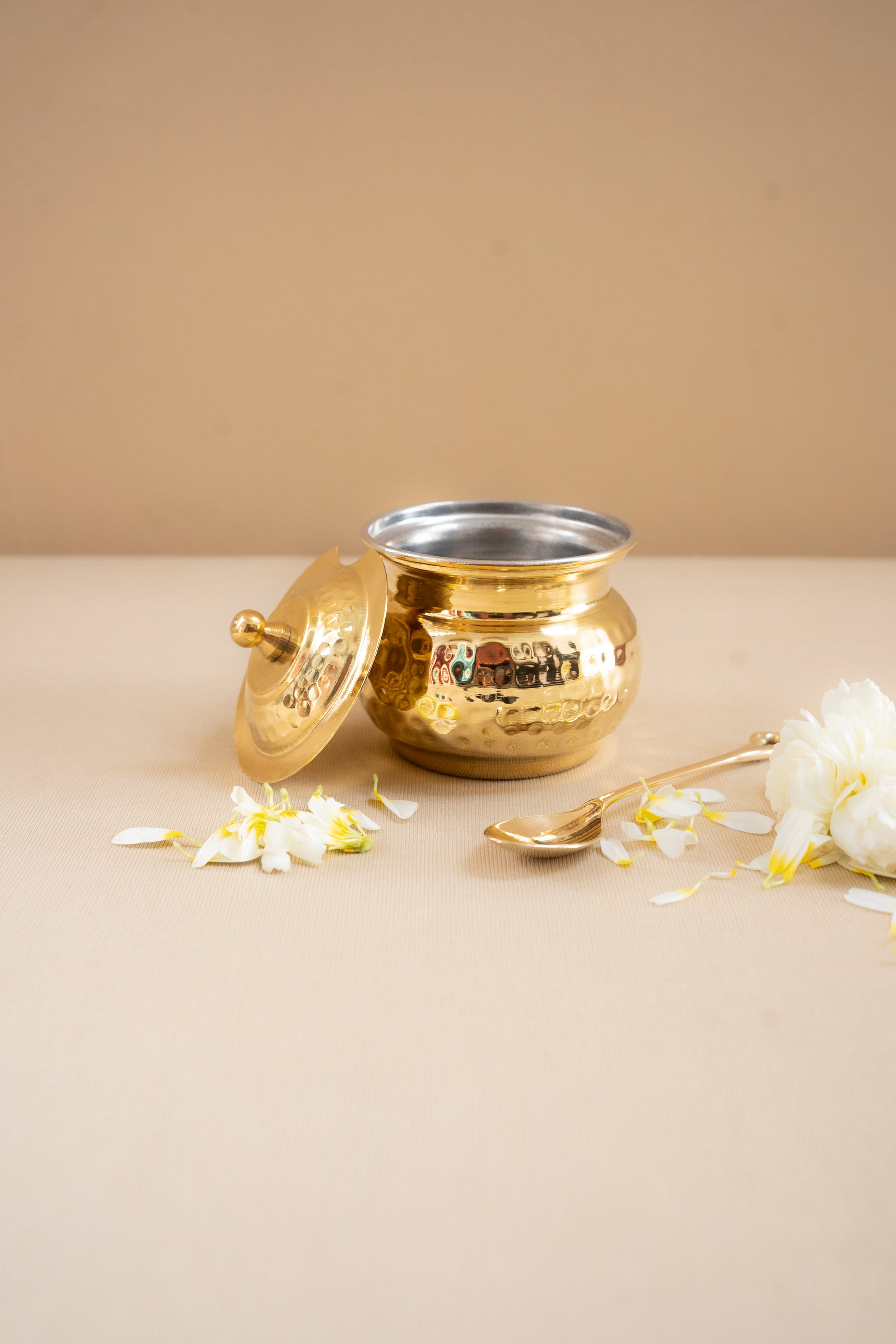 Gold and silver pot with a lid on a beige surface with white flowers.