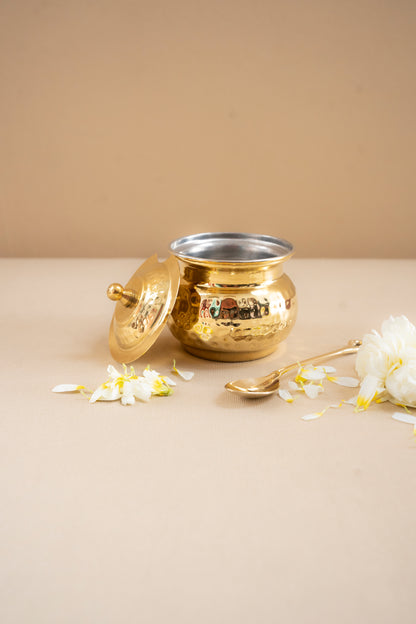 Gold and silver pot with a lid on a beige surface with white flowers.