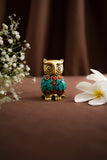 Decorative owl figurine with gemstones on a brown surface with flowers.