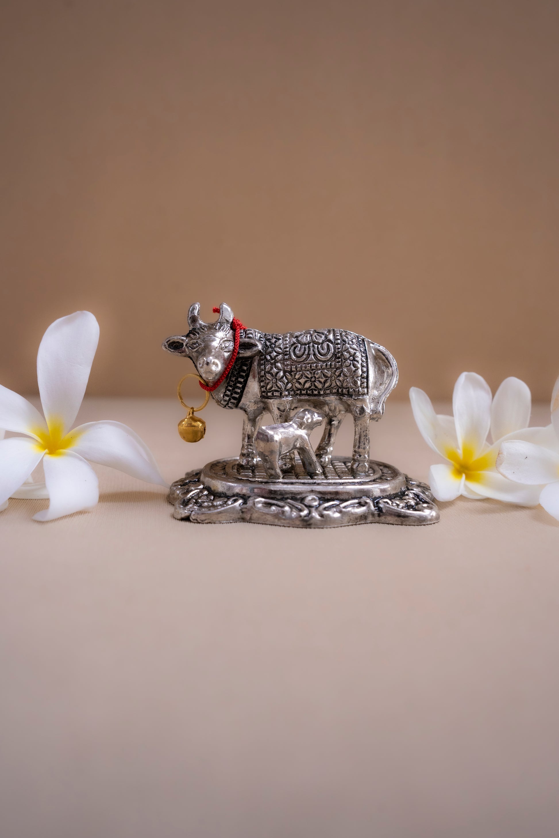 Decorative silver cow figurine with a baby cow on a beige background with white flowers.