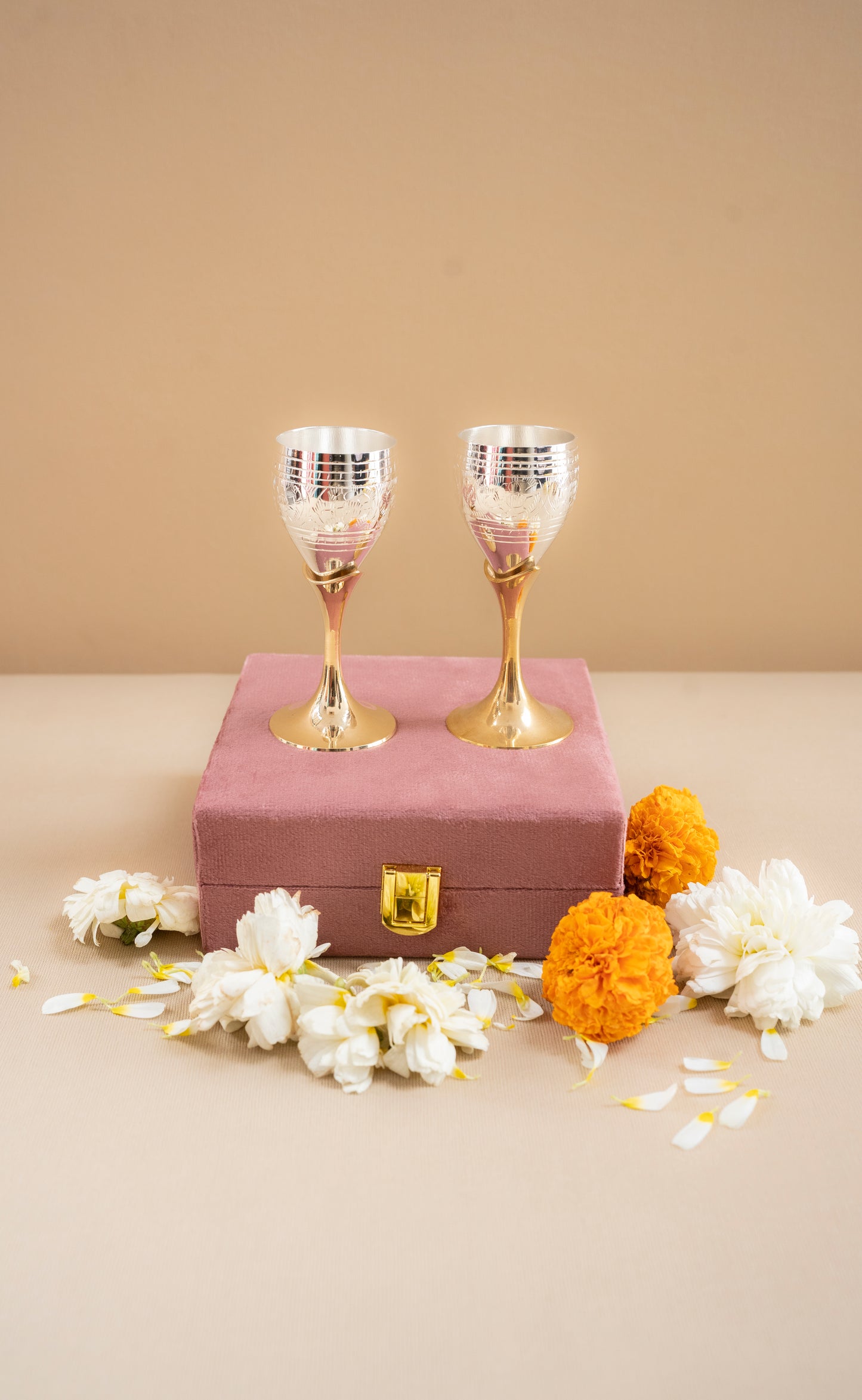 Two gold and silver goblets on a pink box with flowers on a beige background