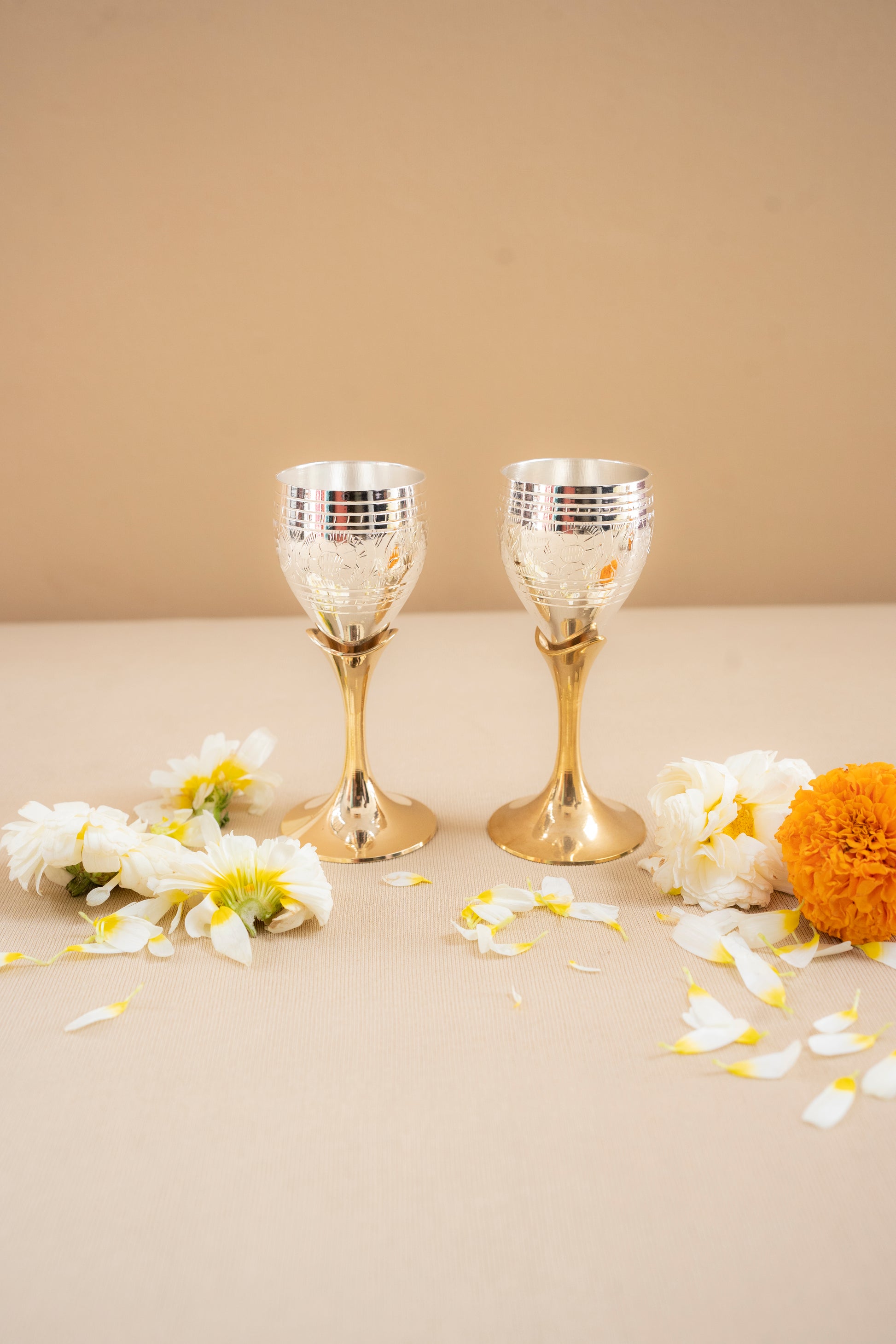 Two gold and silver goblets on a beige surface with flowers around them.