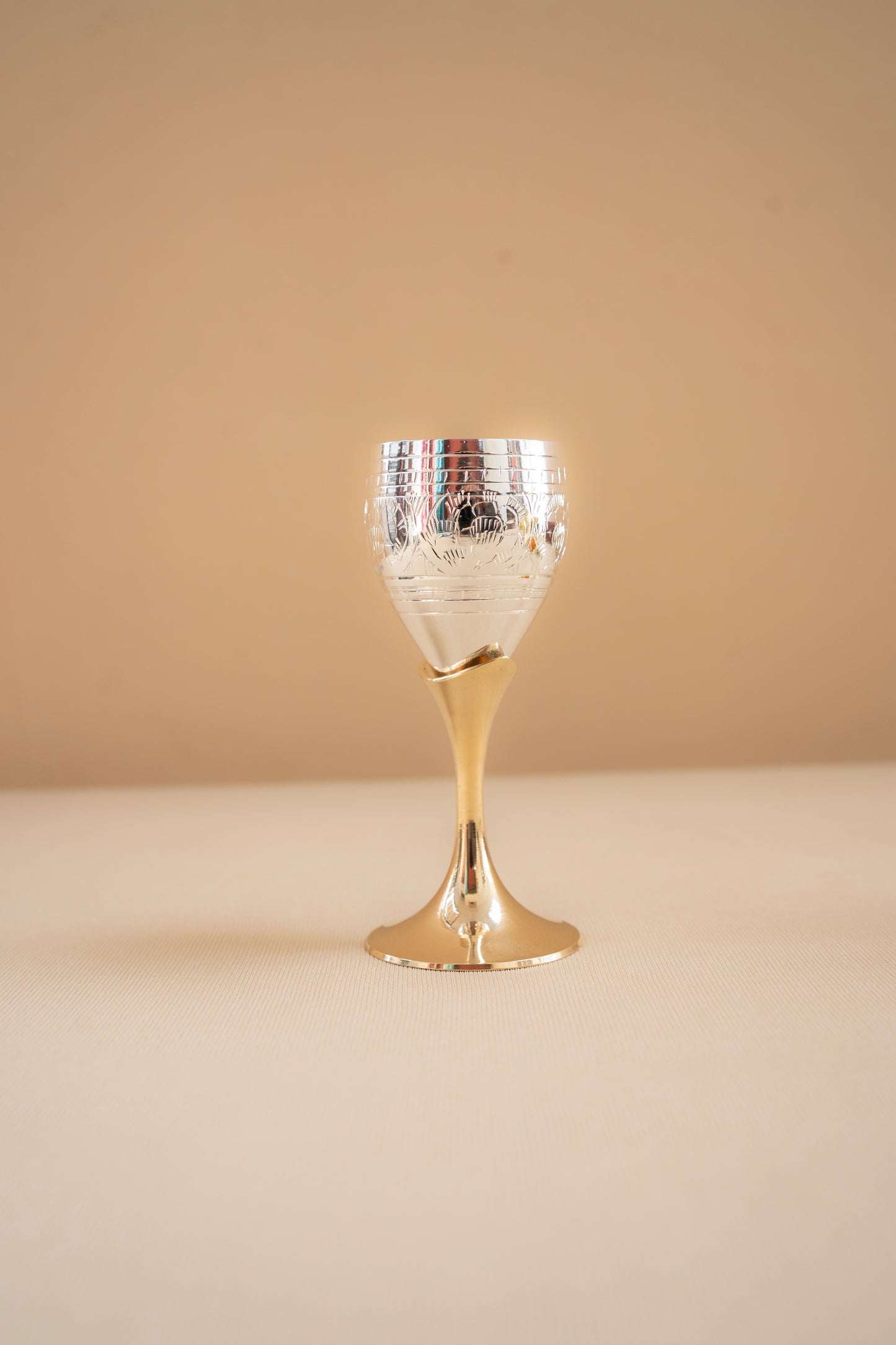 Decorative glass goblet with gold base and silver top on a beige background