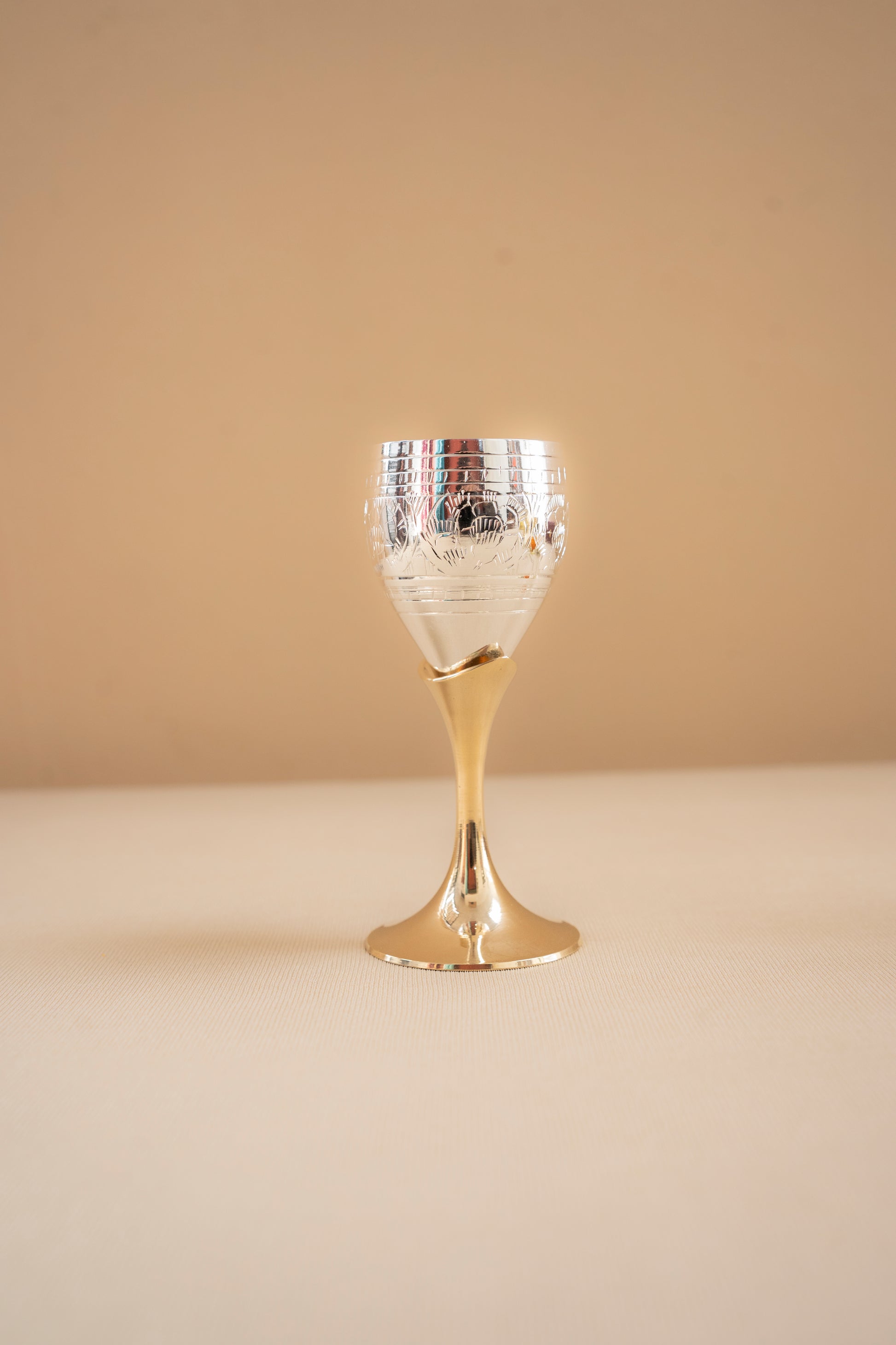 Decorative glass goblet with gold base and silver top on a beige background