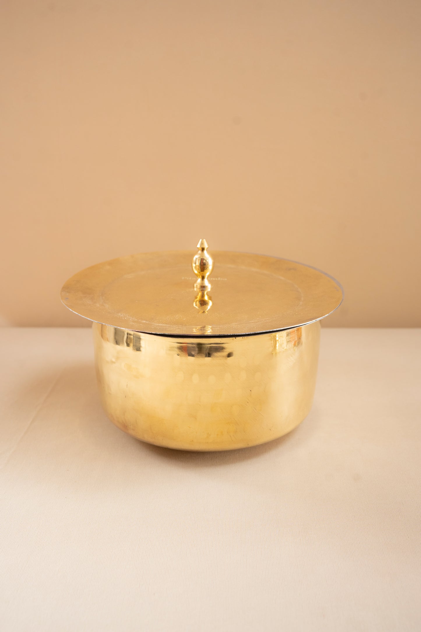 Gold metallic container with lid on a beige surface