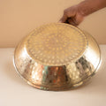 Hand holding a large metallic tray with intricate patterns on a plain background