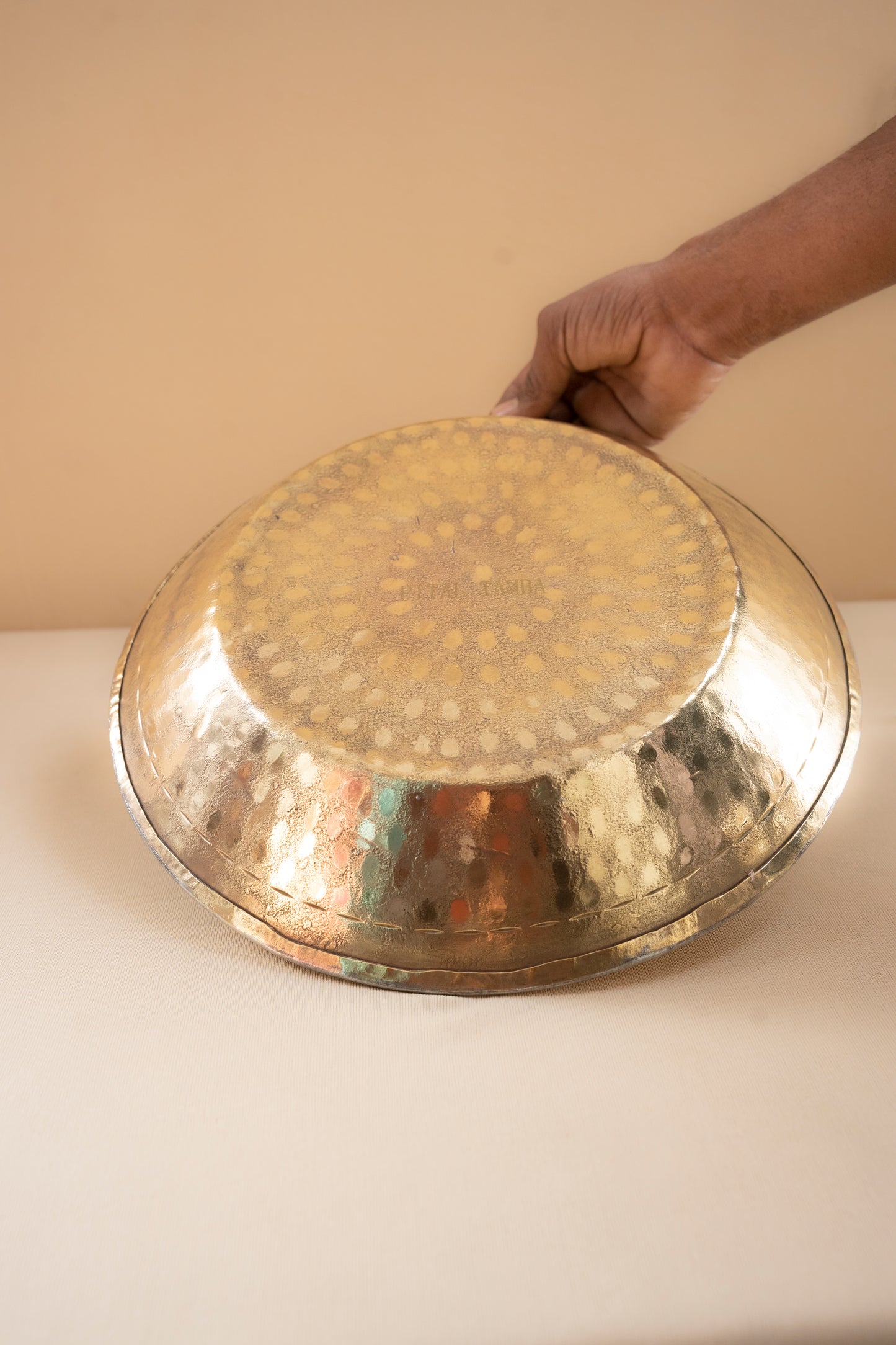 Hand holding a large metallic tray with intricate patterns on a plain background