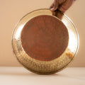 Hand holding a large brass plate against a plain background