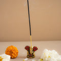 Incense stick with decorative holder on a beige surface with flowers and petals.