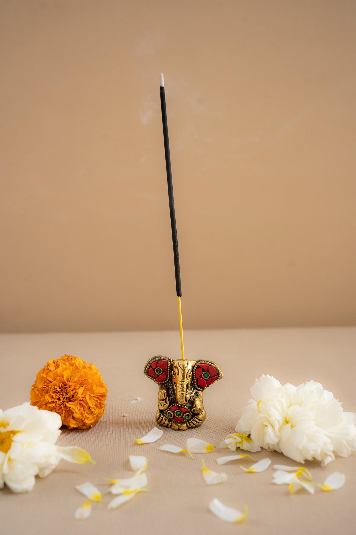 Incense stick with decorative holder on a beige surface with flowers and petals.