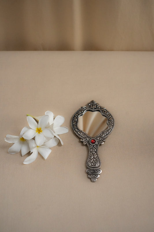 Decorative hand mirror with floral arrangement on a beige background