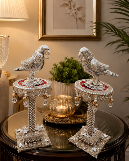 Decorative parrot statues on stands with a candle and plant in the background