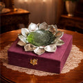 Decorative item with silver lotus design on a purple box on a wooden table.