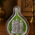 Decorative item with silver figures on a green background, placed on a wooden surface.
