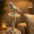 Decorative bird sculpture on a pedestal with a candle and lamp in the background