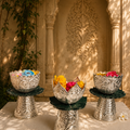 Three silver bowls with colorful flowers on stands against a decorative wall.