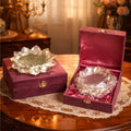 Two silver bowls in open purple boxes on a wooden table with a decorative background.