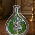 Decorative item with a silver deity figure on a green leaf inside a clear glass container on a wooden surface.