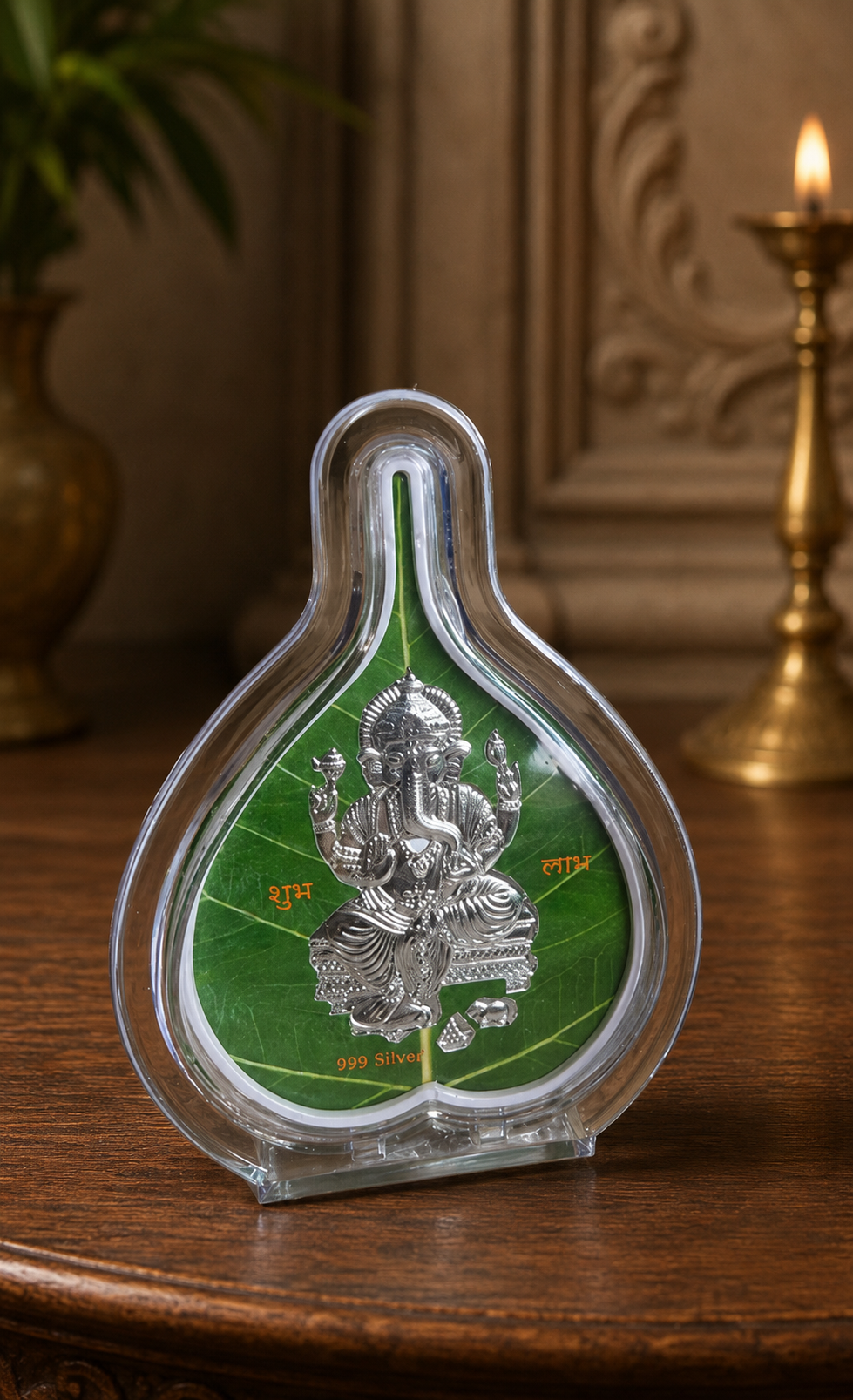 Decorative item with a silver deity figure on a green leaf inside a clear glass container on a wooden surface.