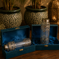 Decorative glass bottles with silver embellishments in blue velvet boxes on a wooden surface.
