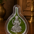 Decorative item with a seated figure on a green leaf in a clear teardrop-shaped frame on a wooden surface.
