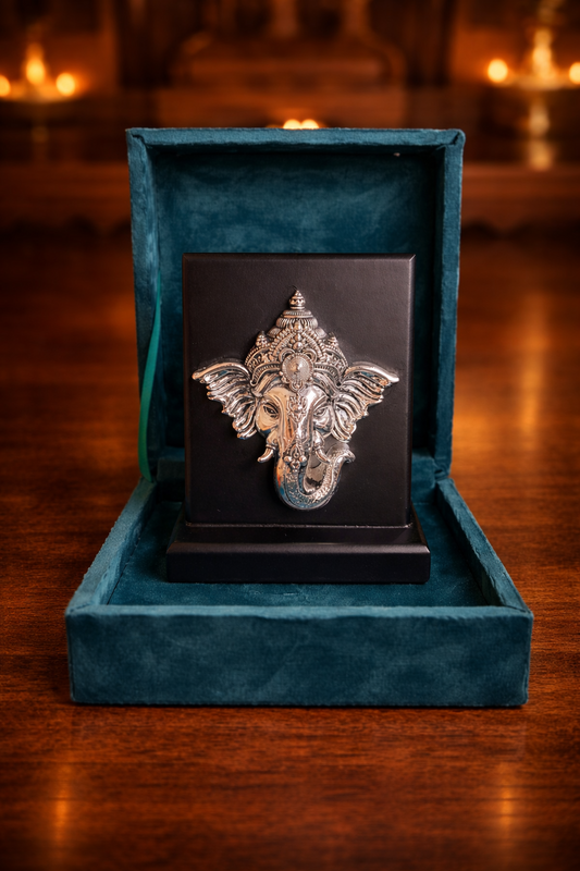 Silver Ganesha statue on a black plaque in a blue velvet box with a warm background.