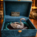 Silver swan ornament in a blue velvet box on a wooden surface.