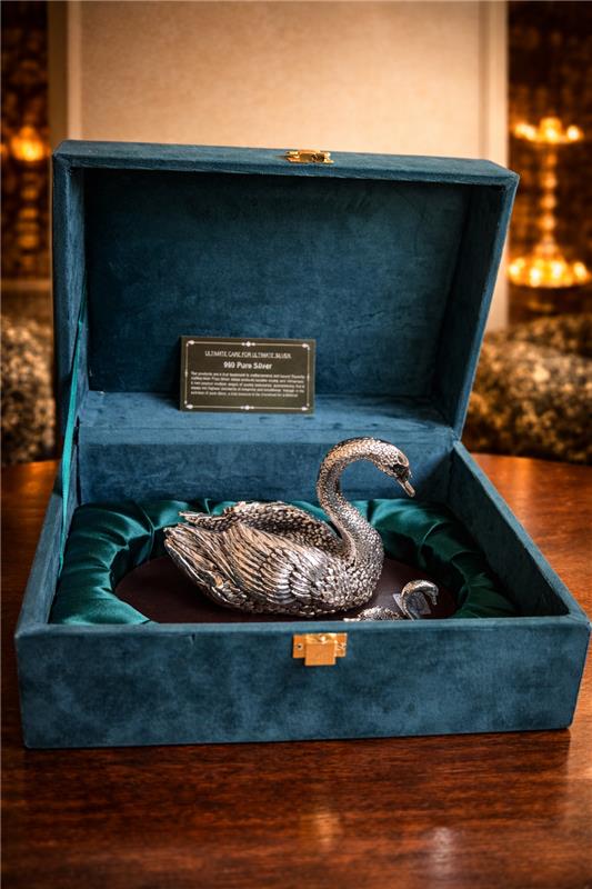 Silver swan ornament in a blue velvet box on a wooden surface.