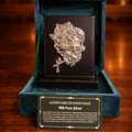 Silver brooch in a green velvet box on a wooden surface with candles in the background
