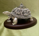 Decorative silver turtle figurine on a wooden base against a green background