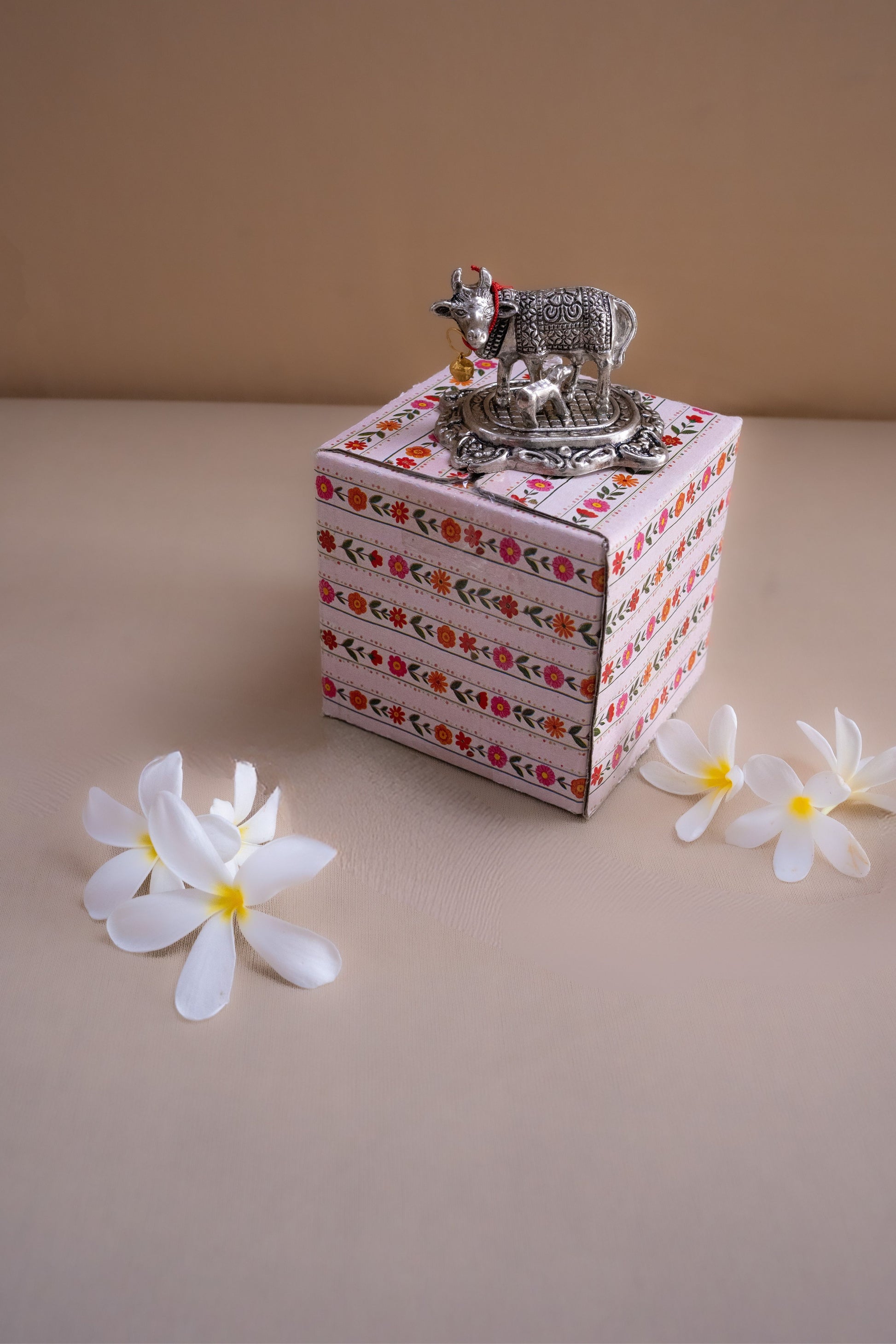 Decorative box with floral patterns and a small decorative item on a beige surface with flowers.