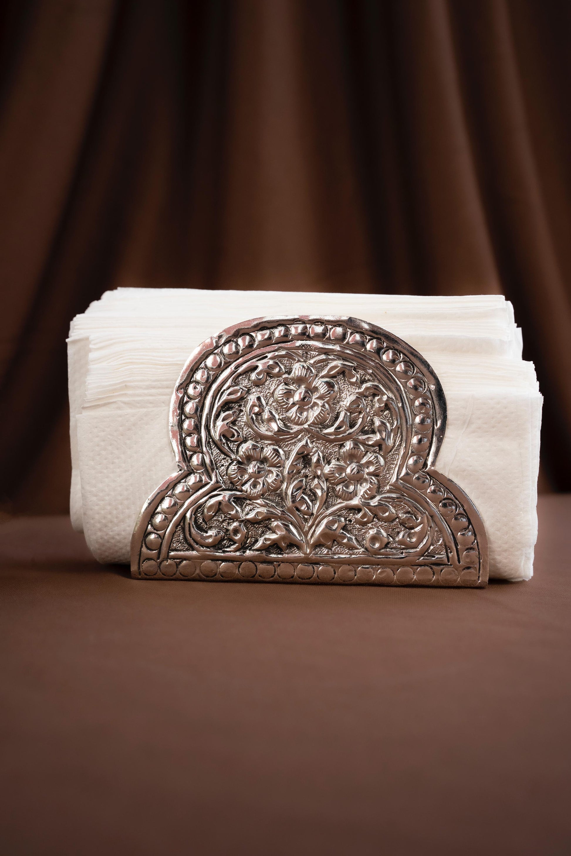 Decorative metal napkin holder with folded white napkins on a brown background