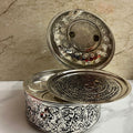 Decorative silver container with intricate designs on a marble surface.