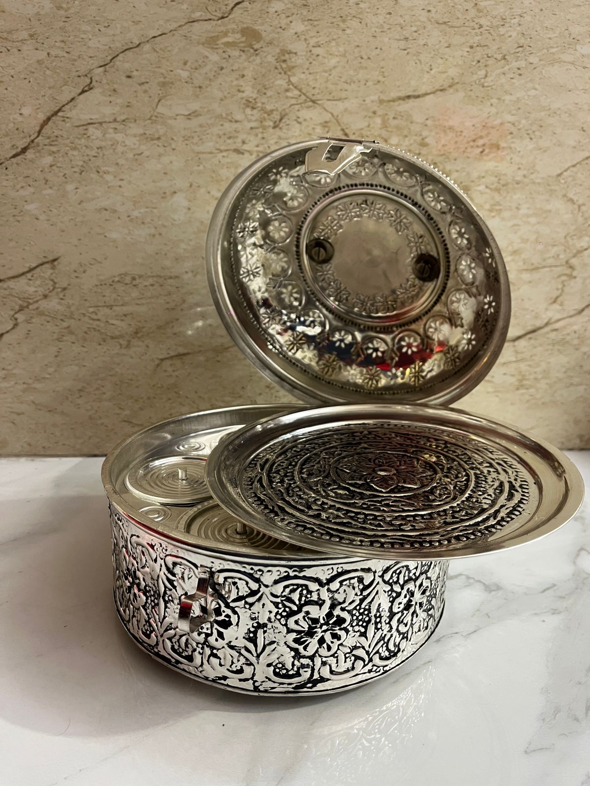 Decorative silver container with intricate designs on a marble surface.