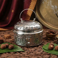 Decorative silver incense burner with burning incense stick on a textured surface.