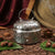 Decorative silver incense burner with burning incense stick on a textured surface.