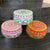 Three colorful round boxes with floral patterns on a dark textured surface