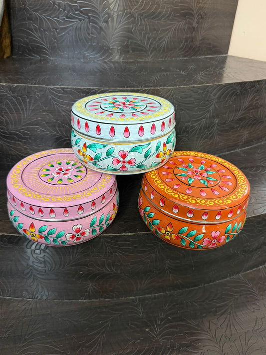 Three colorful round boxes with floral patterns on a dark textured surface